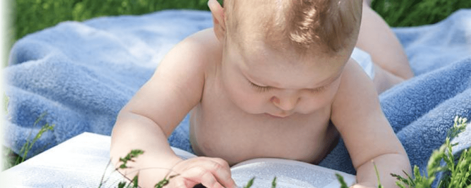 baby exploring a book on a blue blanket outdoors in the grass