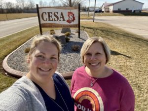 A mentor and her protege are smiling and standing near a large CESA 8 sign.