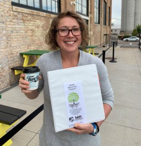 Teacher smiling and holding a cup of coffee in her right hand and the mentor binder in her left hand