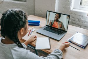 A girl sits at her desk at home while watching her teacher on her laptop